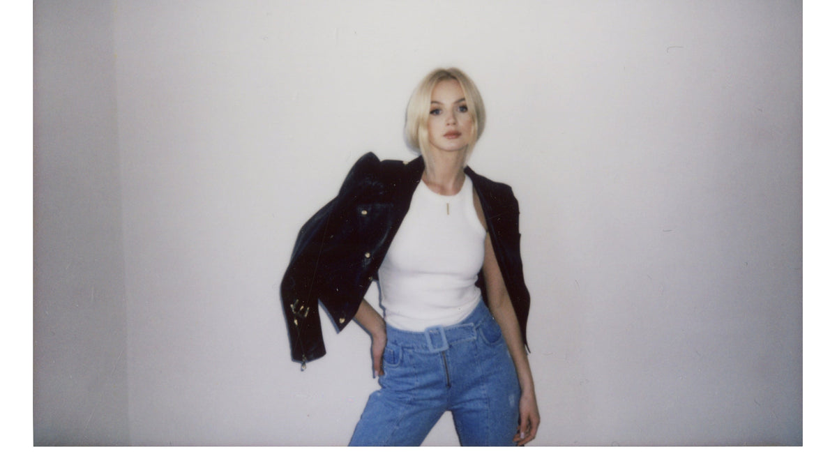 Polaroid of Marlena Janeczko in a black leather jacket and white top, head tilted, against a white wall in a Warsaw studio.