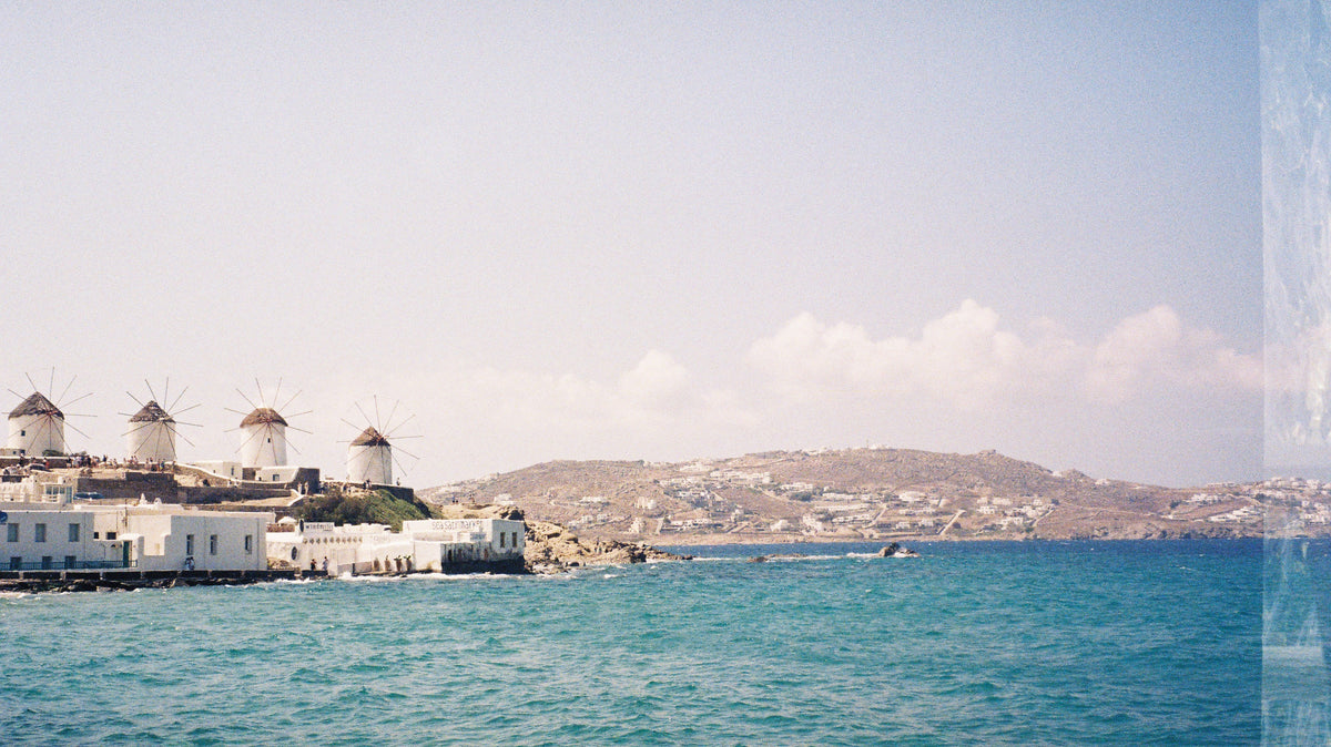 Windmills of Mykonos above white houses and a turquoise sea, shot on 35mm film.