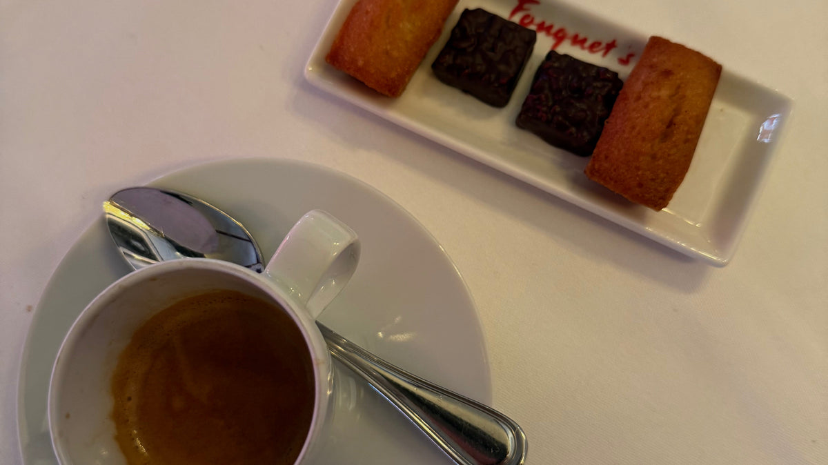 An espresso cup on a white tablecloth next to a plate of madeleines and chocolates at Le Fouquet’s in Paris.