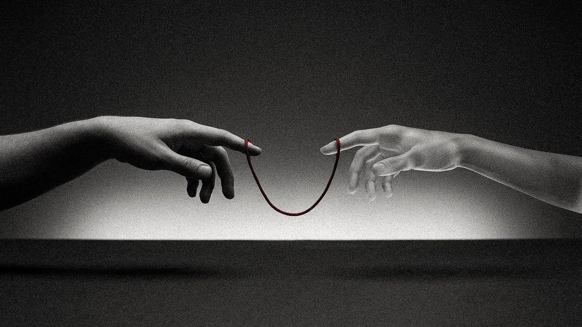 A human hand and a pale sculpted hand reach toward each other against a dark studio background, their index fingers linked by a hanging red thread, echoing Michelangelo's Creation of Adam.