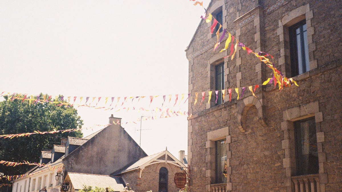 A stone house in Guérande with pink, yellow and violet bunting strung across the street under a pale summer sky.