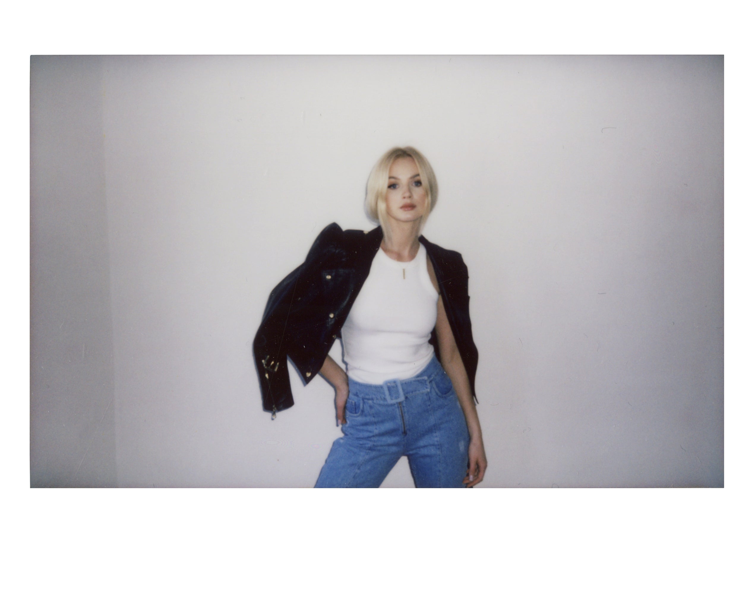 Polaroid of Marlena Janeczko in a black leather jacket and white top, head tilted, against a white wall in a Warsaw studio.