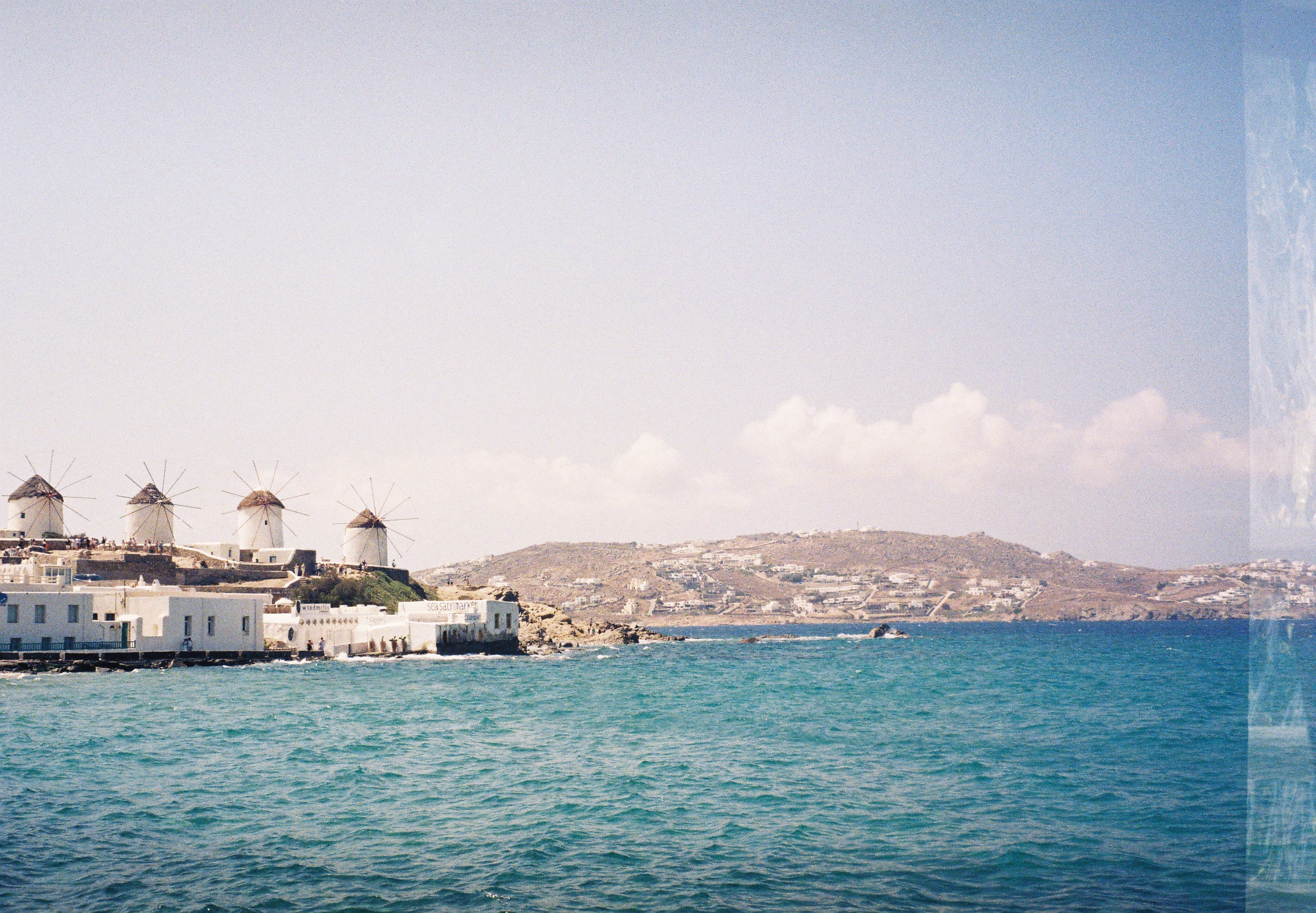Windmills of Mykonos above white houses and a turquoise sea, shot on 35mm film.