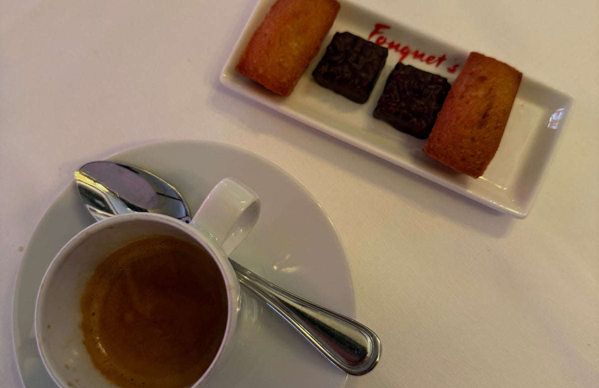 An espresso cup on a white tablecloth next to a plate of madeleines and chocolates at Le Fouquet’s in Paris.