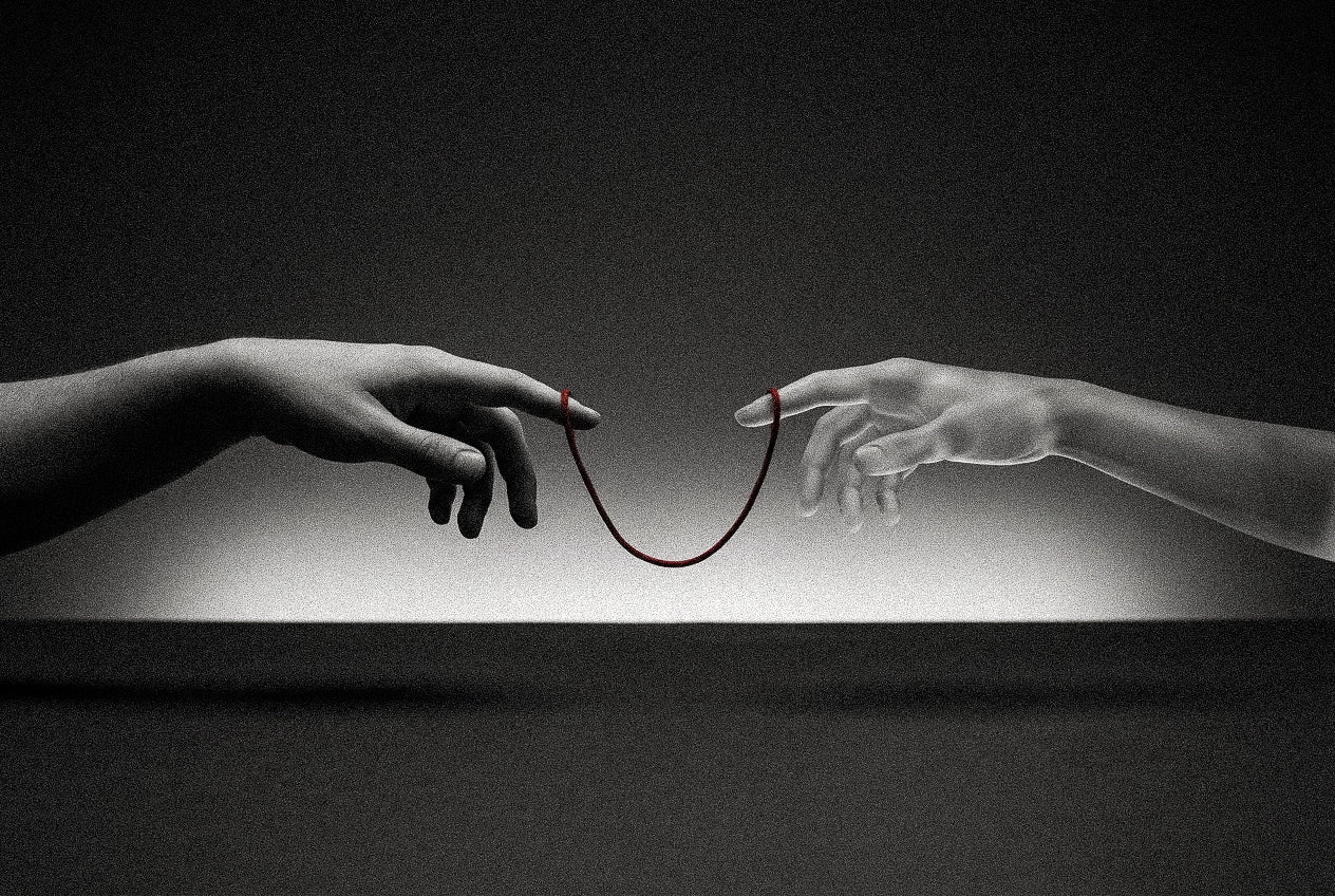 A human hand and a pale sculpted hand reach toward each other against a dark studio background, their index fingers linked by a hanging red thread, echoing Michelangelo's Creation of Adam.