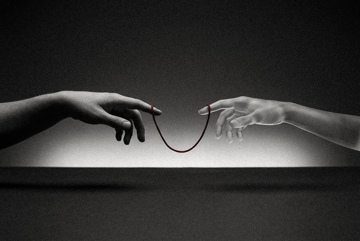 A human hand and a pale sculpted hand reach toward each other against a dark studio background, their index fingers linked by a hanging red thread, echoing Michelangelo's Creation of Adam.