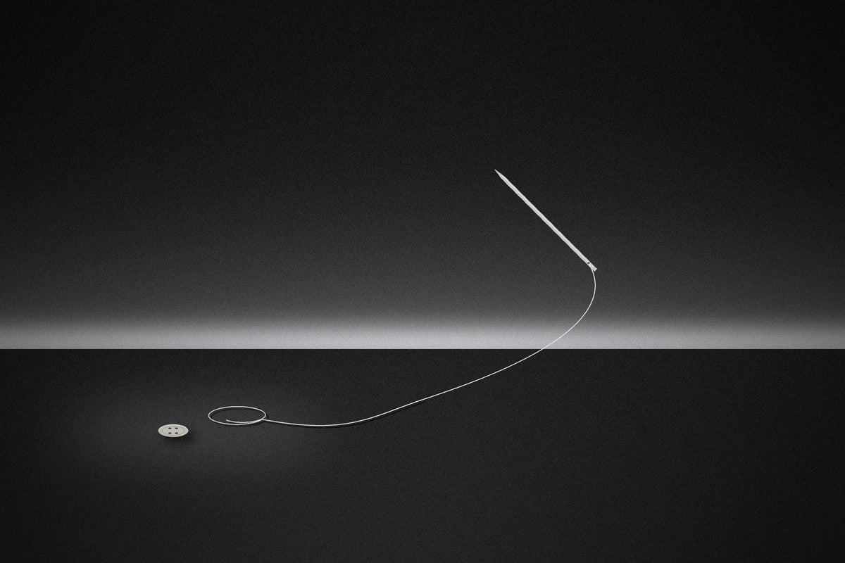 A needle and thread floating above a dark table, beside a single button